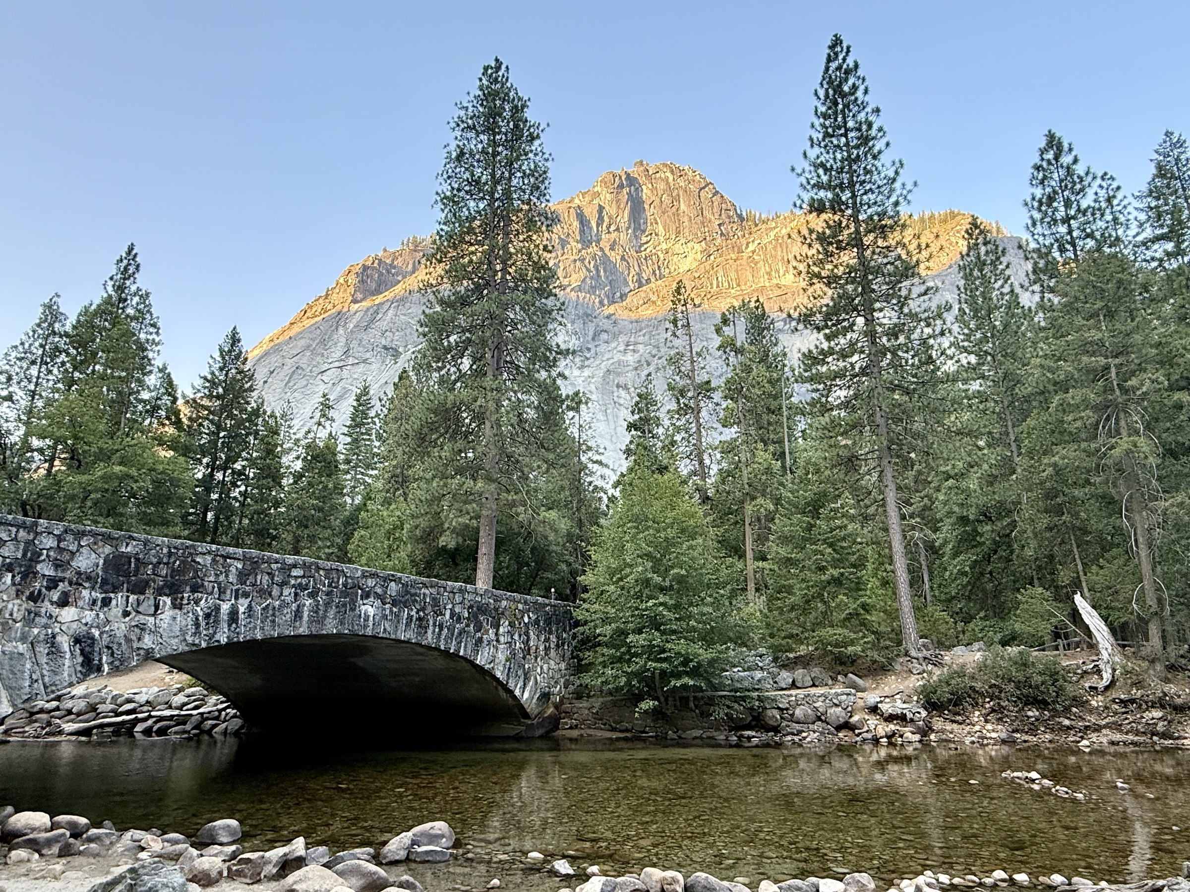 A stone bridge and Yosemite cliffs illuminated by evening light